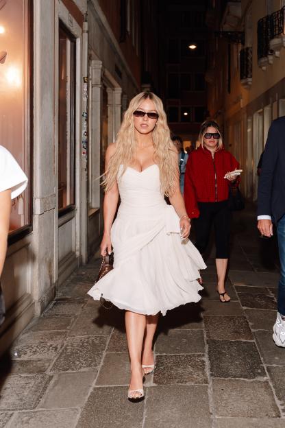 Sydney Sweeney in a white Chanel dress and sunglasses walking down a narrow street in Venice.