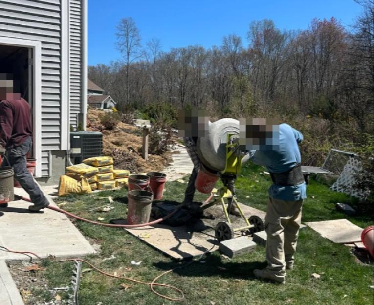 Two men operating a cement mixer near a house under construction.