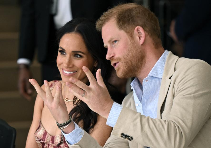 Prince Harry speaking and Meghan Markle smiling while attending a show.
