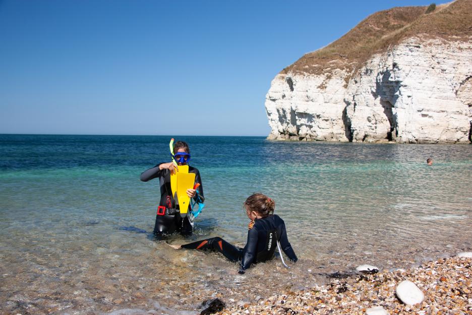 Two snorkelers on a clear water beach with white cliffs in the background.