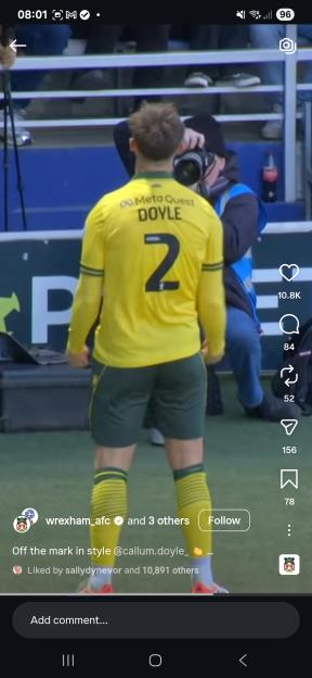 A soccer player in a yellow and green uniform with "Doyle" and the number "2" on the back, being photographed by a person in the background.