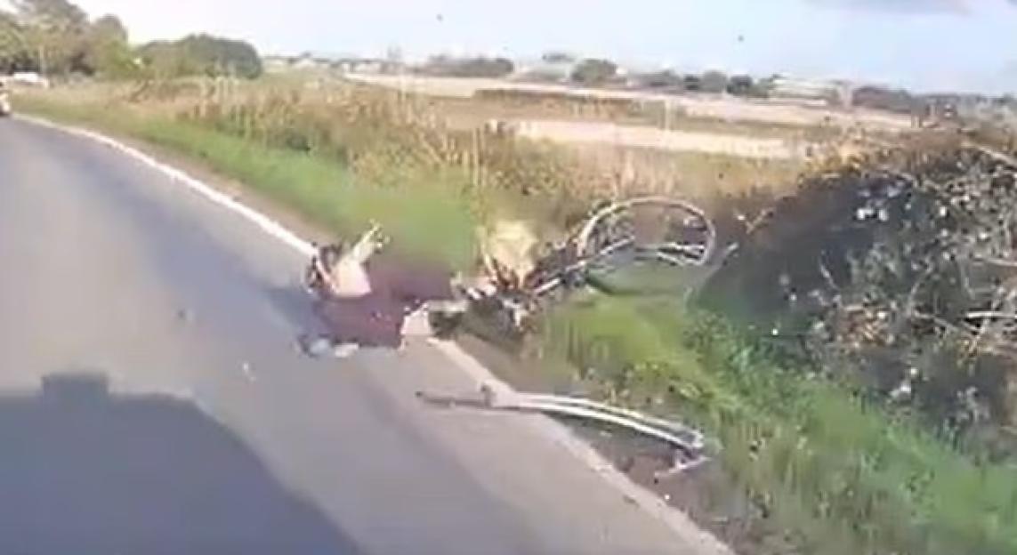 A person lying injured on the roadside next to a damaged bicycle.
