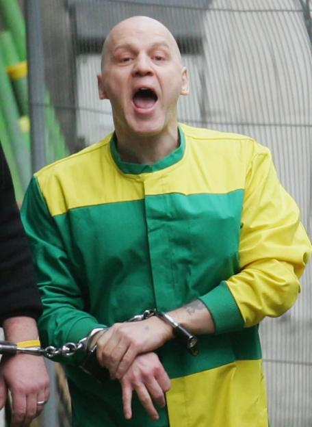 Convicted murderer Michael Stone yells while handcuffed, wearing a green and yellow jumpsuit.