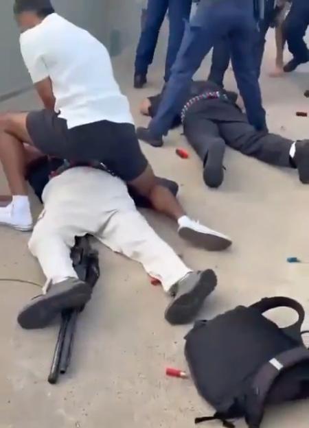 Suspects detained on the ground with a firearm and shotgun shells nearby.