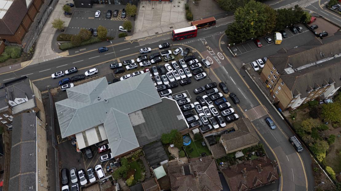 Aerial view of a dealership with numerous cars parked on pavements and double yellow lines, overflowing into nearby streets.