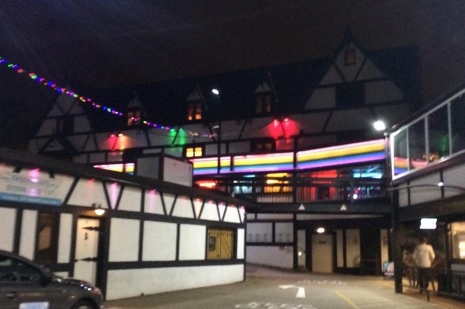 Exterior view of Pink Punters nightclub in Milton Keynes at night, with Tudor-style architecture illuminated by colorful lights.