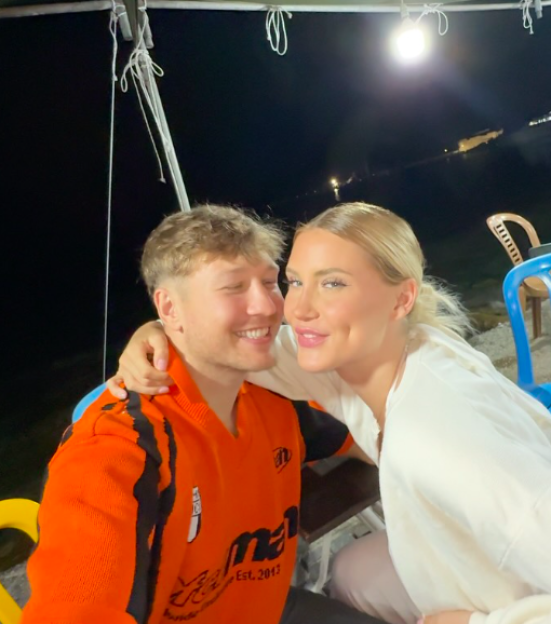 A man in an orange shirt and a woman with blonde hair smiling at the camera at night.