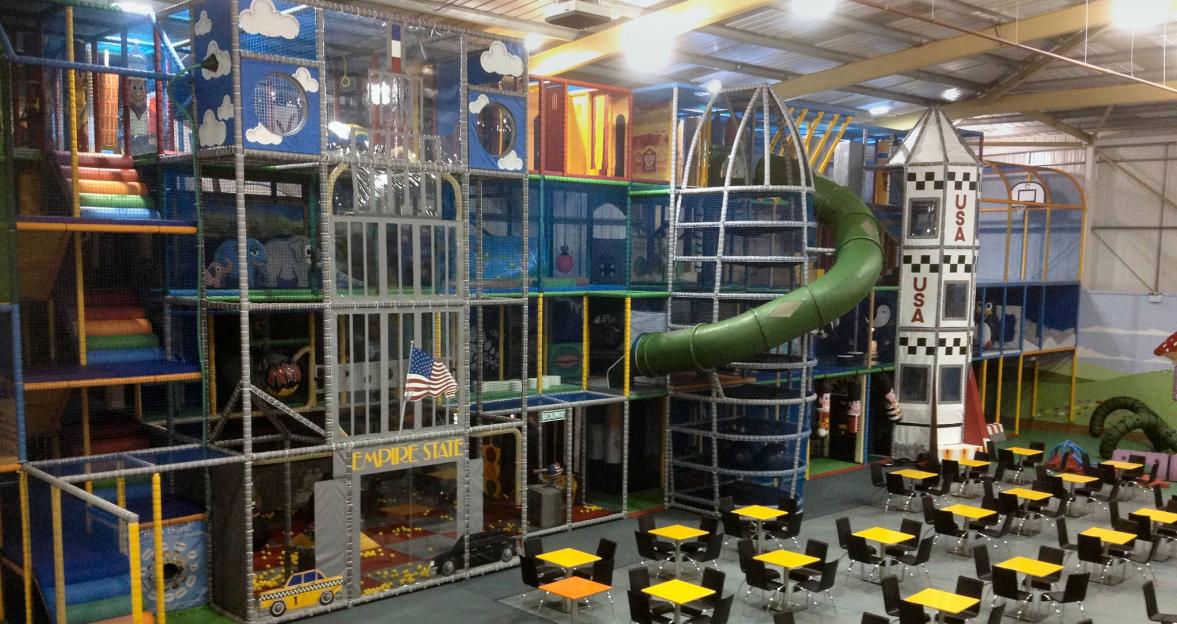The Riverside Hub in Northampton features a large indoor play area with slides, climbing structures, and a separate seating area with tables.