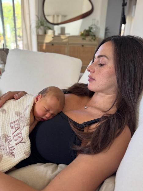 A newborn baby wrapped in a blanket sleeps on its mother's chest.