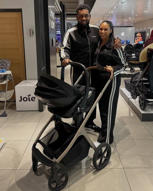 A smiling man and woman stand next to a baby carriage in a store.