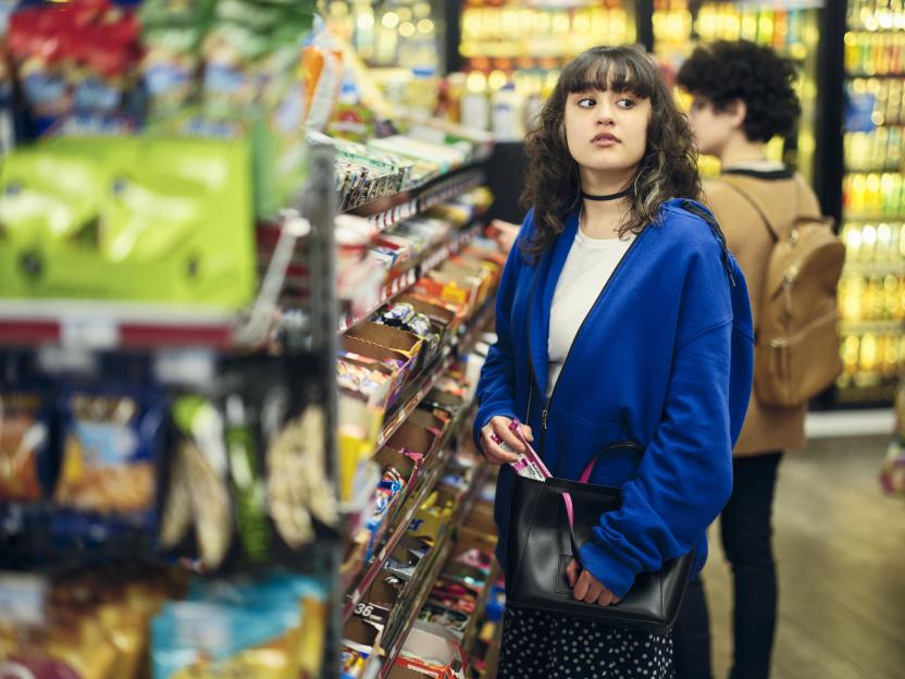 A young woman placing merchandise into her purse in a convenience store.