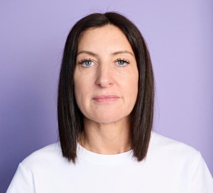 A woman with dark hair and blue eyes, wearing a white t-shirt, looking directly at the camera.