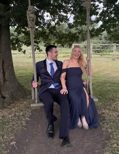 Tom Davies and his girlfriend Alex Ross sitting on a swing under a tree, laughing.