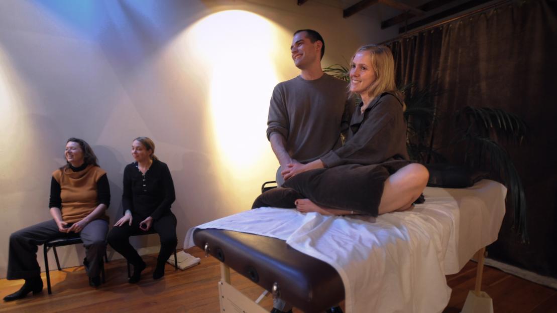 Justine Dawson on a massage table with a man, and two other women sitting to the left.
