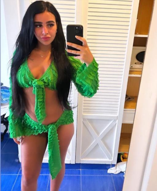 A woman in a green two-piece outfit takes a selfie in a mirror.