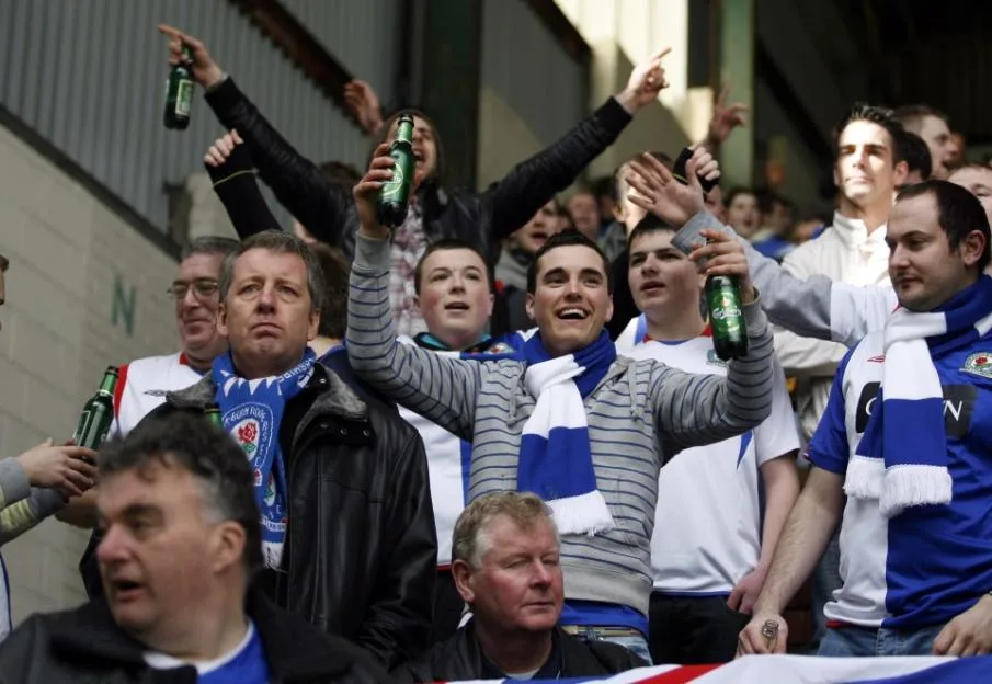 Blackburn Rovers fans holding up bottles of beer inside a stadium.