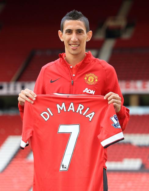 Footballer Angel di Maria holds up a Manchester United jersey with his name and the number 7 on it, at Old Trafford stadium.