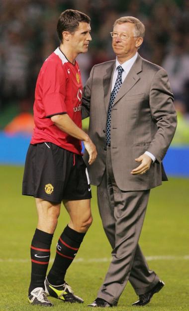 Roy Keane in a red Manchester United kit with Alex Ferguson in a suit during Keane's testimonial match.