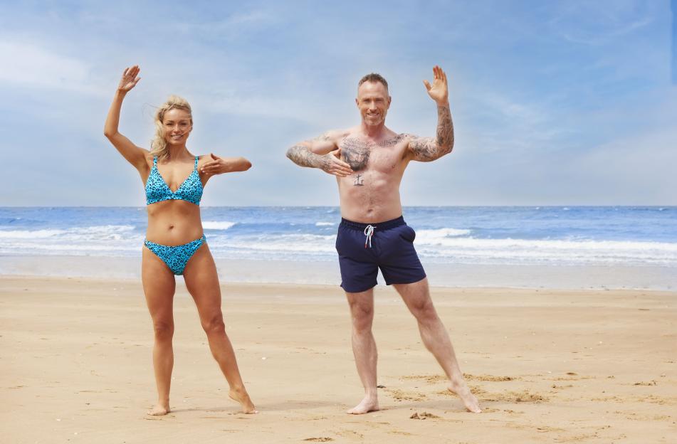 Ola and James Jordan on a beach, smiling with arms raised.