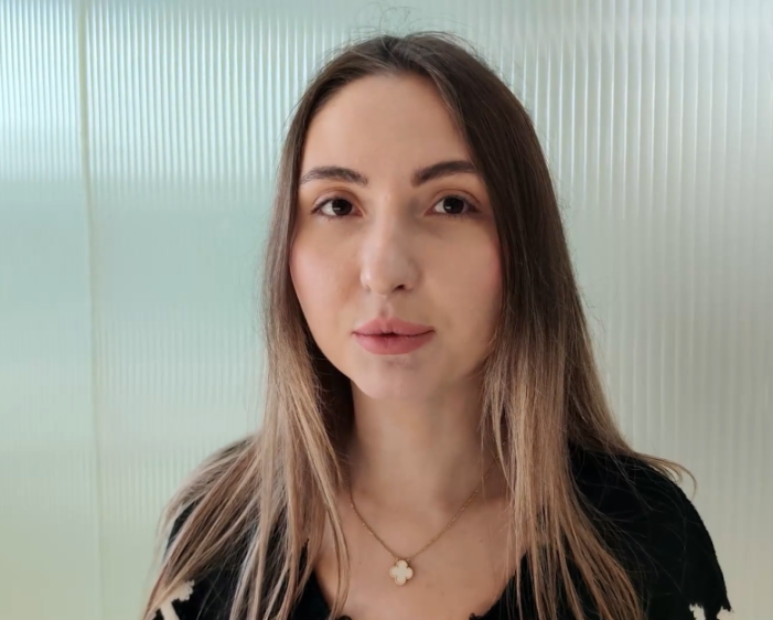 A woman with long brown hair and a clover-shaped necklace.
