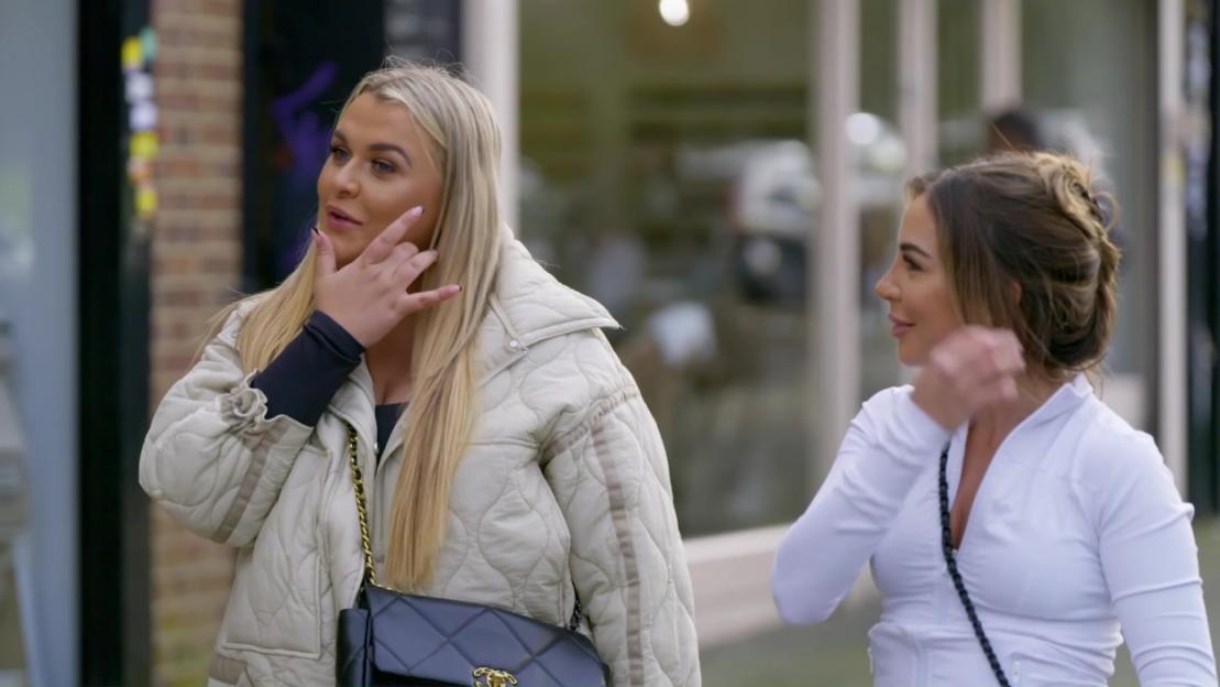 Two women standing outdoors, one making a hand gesture.
