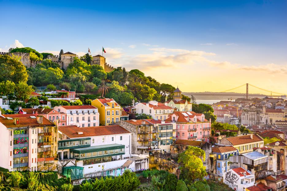Lisbon cityscape at dusk, with a castle and bridge in the distance.