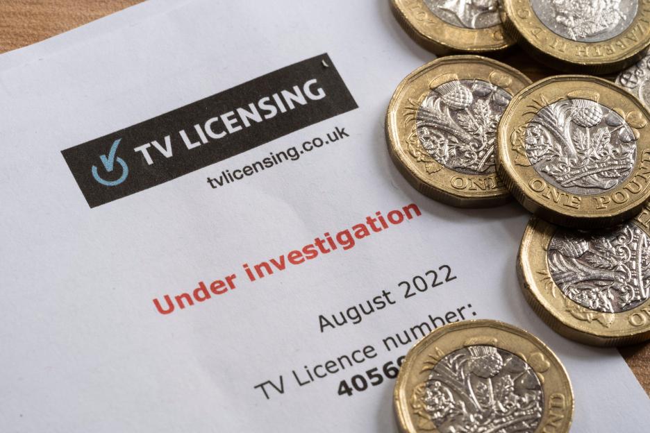 A letter from TV Licensing stating "Under investigation" for August 2022, with several one-pound coins scattered on it.