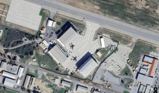 Satellite view of an airport with several aircraft visible near hangars and an airfield runway.