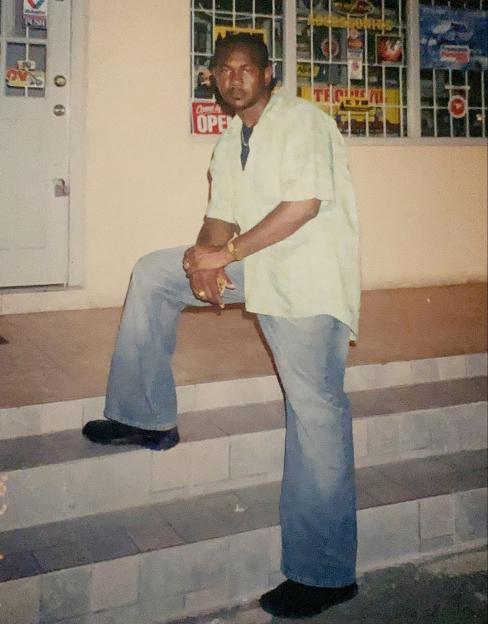 A man stands on stone steps outside a building, wearing a light-colored shirt, jeans, and black shoes.