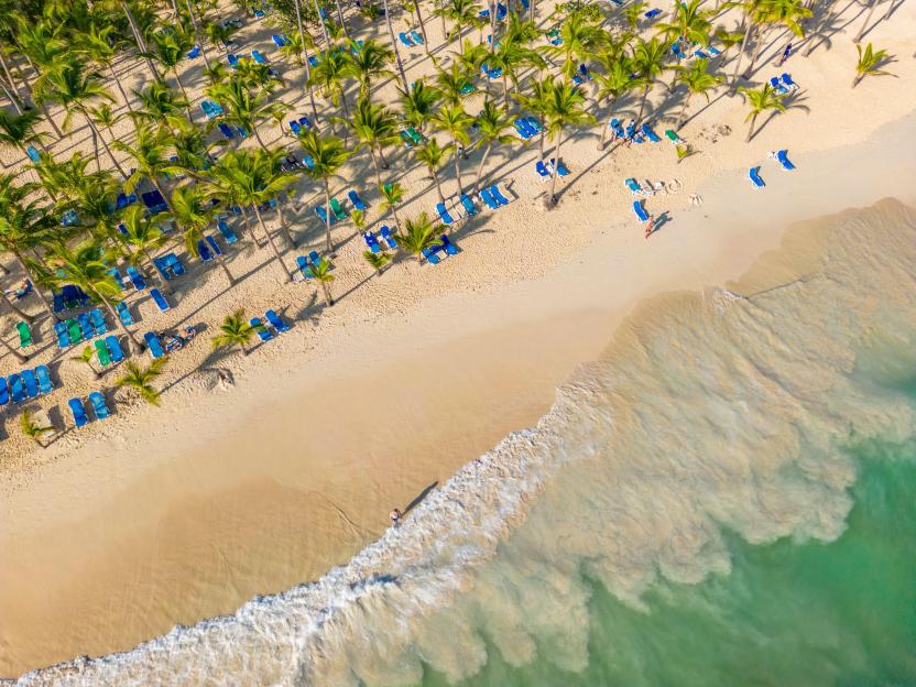Aerial view of Bavaro Beach in Punta Cana, Dominican Republic, showing palm trees, lounge chairs, and people by the ocean.