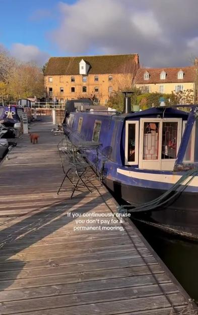 A blue canal boat docked next to a wooden pier with houses in the background.