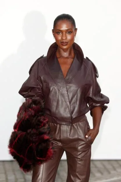 Model poses in a chocolate brown leather jacket and trousers with a red and black furry accessory.