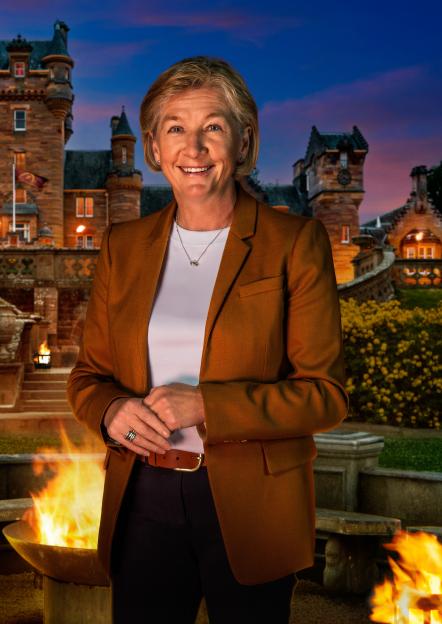 Amanda, a 57-year-old retired police detective, smiling in front of a castle at dusk, with a fire pit in the foreground.