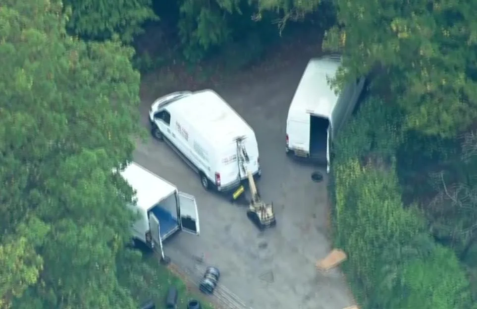 Aerial view of a wheeled robot operating near three parked white vans during a counter-terrorism investigation.
