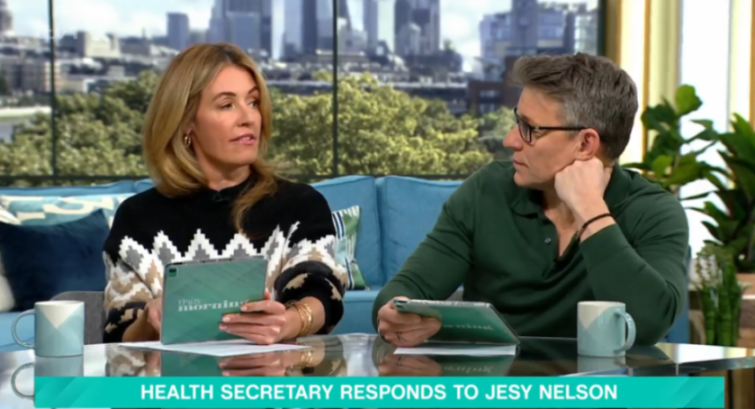 Two TV presenters, a woman and a man, sit on a teal couch, each holding a tablet, with a banner at the bottom reading "HEALTH SECRETARY RESPONDS TO JESY NELSON."