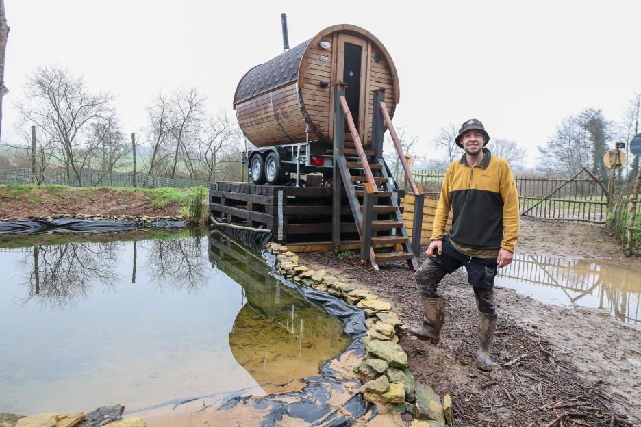 Sam Griffiss standing next to a barrel-shaped sauna on a trailer.