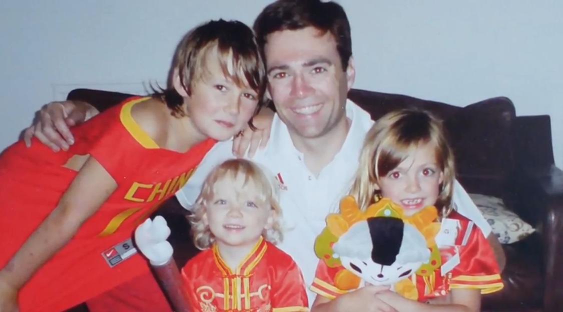 Andy Burnham smiling with his arm around a boy, while two younger children sit in front.