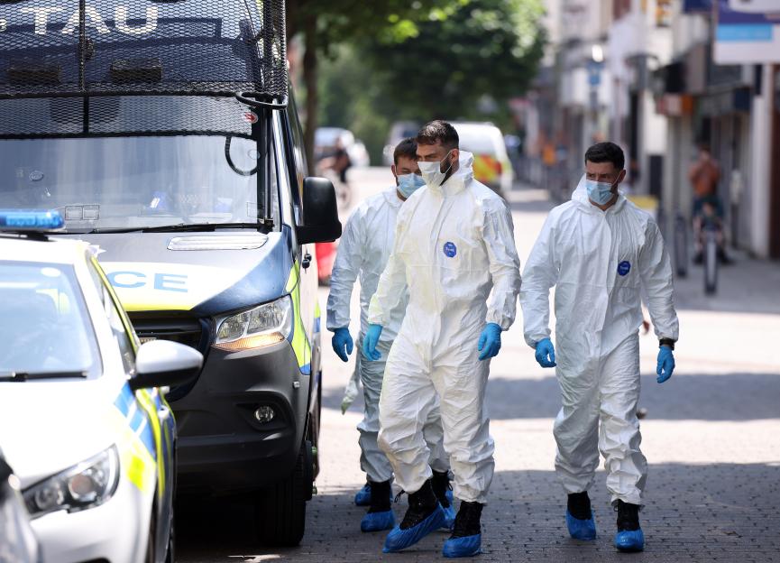 Forensic officers in white suits and masks near a police van at a crime scene.