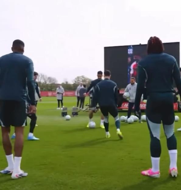 Soccer players training on a field with a large screen displaying another soccer player.