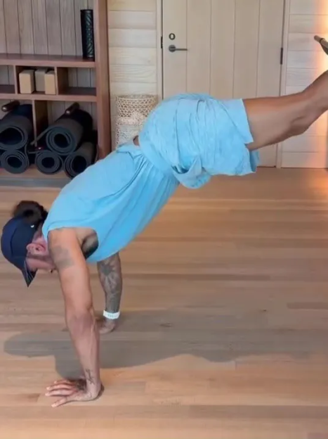 Man in a blue shirt and shorts doing a handstand.