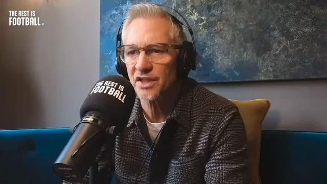 A man with gray hair, glasses, and headphones speaks into a microphone labeled "The Rest Is Football."