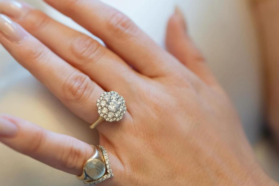 Tabitha Willet's engagement ring, a gold ring with a large cluster of diamonds, on her finger, next to another gold ring with a large flat oval stone surrounded by small diamonds.