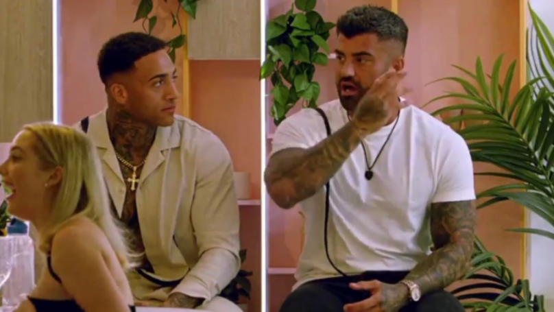 Three people, two men and a woman, react to a conversation in what appears to be a casual indoor setting with plants in the background.