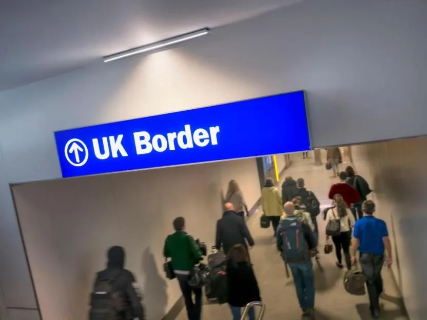 Passengers walking through an airport terminal beneath a blue UK Border sign.