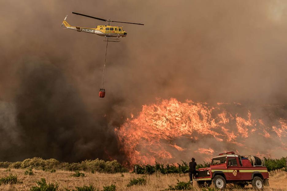 A Working On Fire Bell Huey similar to the one that crashed after its rotors hit a mountain in Hout Bay, South Africa, on a different fire dropping water from the 1000 litre bucket below to help put out a South African wildfire