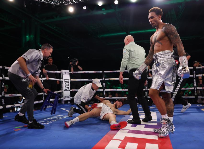 Ben Whittaker, in silver shorts, stands over Benjamin Gavazi, who is knocked out on the mat.