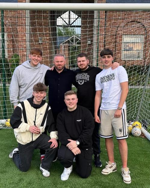 Wayne Rooney with five other men in front of a soccer goal.