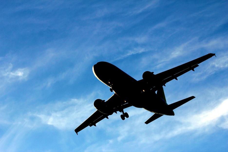Silhouette of a plane landing against a cloudy blue sky.