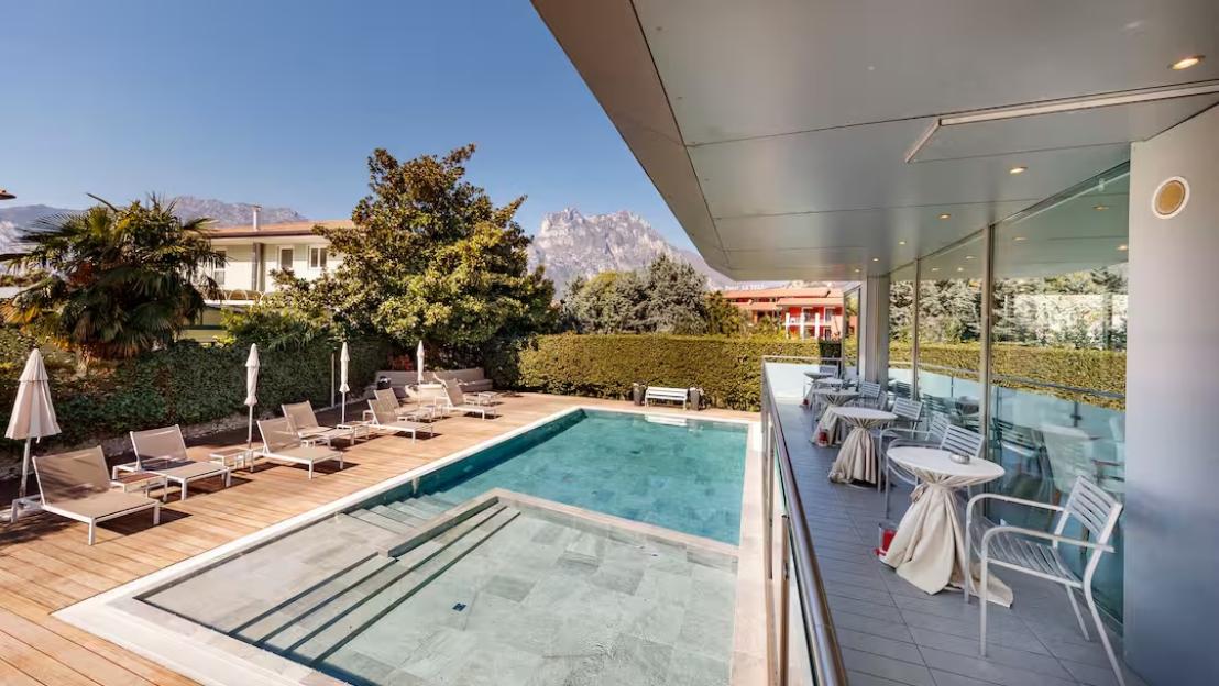 An outdoor swimming pool surrounded by lounge chairs and umbrellas, next to a modern building with a covered patio and outdoor seating.
