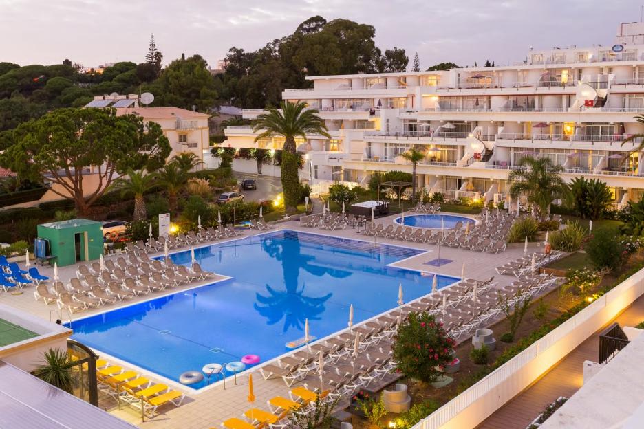 An aerial view of the Muthu Clube Praia da Oura hotel with a swimming pool at dusk.